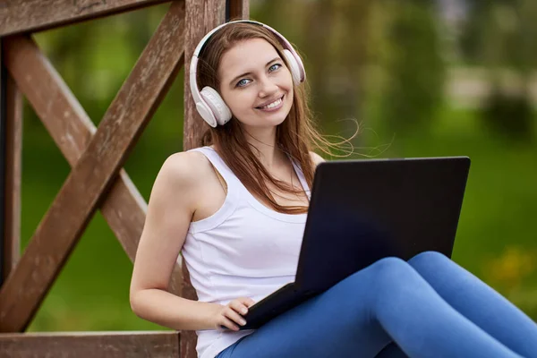 Lächelnde Frau mit Kopfhörer und Laptop draußen. — Stockfoto