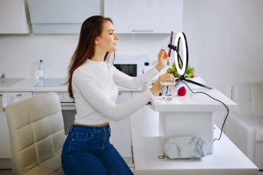 Güzellik blogcusu evde canlı yayın sırasında cep telefonu tutacağı ile halka ışığı kullanıyor.