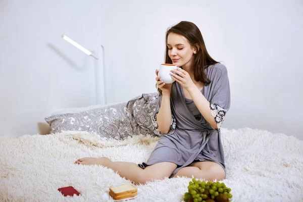 Snídaně do postele od mladé bílé ženy s šálkem kávy v ruce. — Stock fotografie
