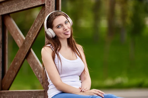 Vrouw in draadloze koptelefoon toont tong in het openbaar park. — Stockfoto