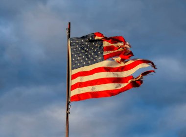 Gökyüzüne karşı batan güneşin ışınlarında eski püskü Amerikan bayrağı