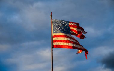 Gökyüzüne karşı batan güneşin ışınlarında eski püskü Amerikan bayrağı