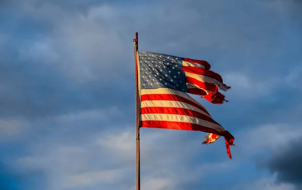 Gökyüzüne karşı batan güneşin ışınlarında eski püskü Amerikan bayrağı