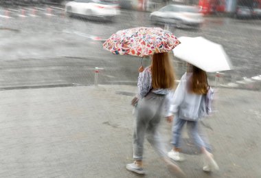 Blurred image of two girls with umbrella walking in the rain down the street