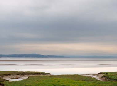 Kumsaldaki kumların üzerindeki kumların üzerindeki kıyı manzarası ön planda çimlerle kaplı sulak alanlar ve uzaklıktaki kuzey gölleri.