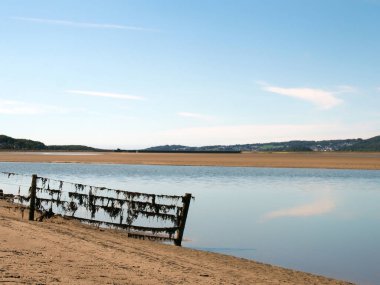 Kent nehri Cumbria 'da, Arnside yakınlarında. Uzaktaki Lakeland köyleri ve güneş mavisi gökyüzü suya yansıyor.
