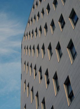 Parlak mavi gökyüzüne karşı beyaz taş kaplama ve çapraz pencereli modern bir apartman gelişimi perspektifini kapat