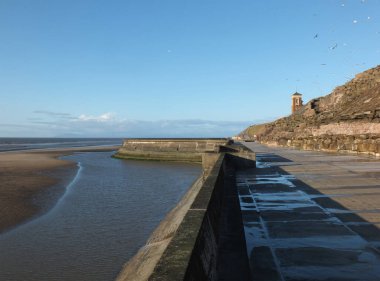Sahildeki kayalıklarda beton merdivenler. Blackpool 'da, kumsalda, güneş batarken. Eski tekne havuzu ve kule farklı.