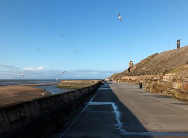 Sahildeki kayalıklarda beton merdivenler. Blackpool 'da, kumsalda, güneş batarken. Eski tekne havuzu ve kule farklı.