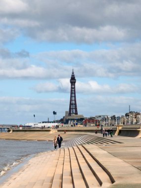 Blackpool, Lancashire, Birleşik Krallık - 5 Mart 2022: Güneyden siyah havuz manzaralı merdivenlerde dalgalar kırılıyor, insanlar gezinti güvertesinde ve altın milde ve uzaktaki kulede