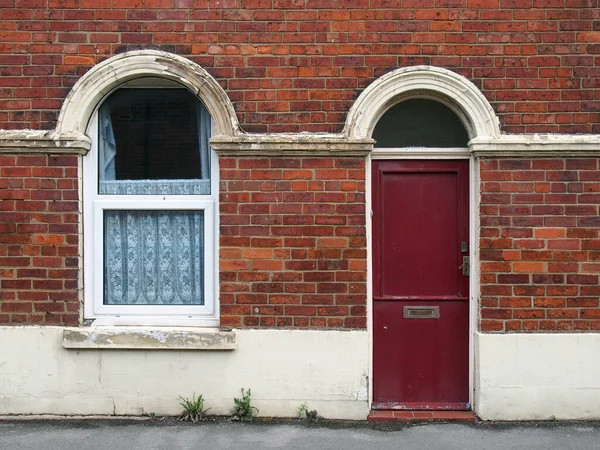 赤いフロントドアとみすぼらしい剥離塗装で典型的な古いレンガ造りの英国のテラスハウスの窓 — ストック写真