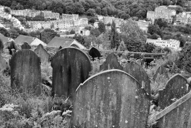 gravestones overgrown with weeds overlooking the town of hebden bridge at the disused cross lanes former methodist burial ground