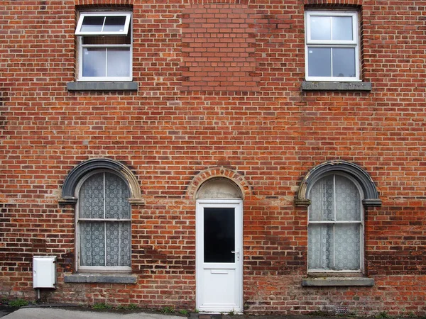 アーチ型の窓とネットカーテンを備えた典型的な古いレンガ造りの英国のテラスハウスの白いフロントドアと窓 — ストック写真
