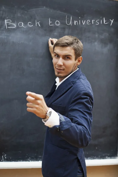 Young teacher writing on a blackboard with chalk — Stock Photo, Image