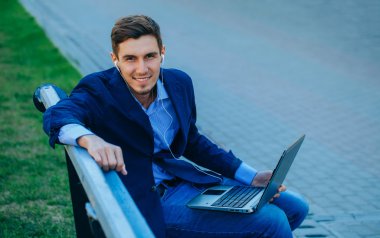 Mutlu iş adamı dışarıda bankta dizüstü bilgisayar kullanıyor.