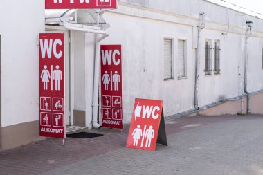 Beyaz bir binanın arka planında umumi tuvaletlerin kırmızı işareti