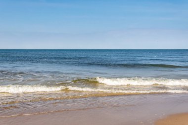 Sarı kum ve mavi gökyüzünün arka planında deniz dalgaları