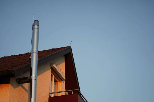 Residential house roof with new outdoor metal chimney. A new gas heater provides hot water and heats the house on cool days