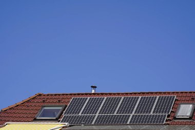 Çatı pencereleri arasındaki fayanslı çatıda güneş modülleri. Parlak güneş ışığı ve bulutsuz gökyüzü yüksek elektrik üretimini garanti ediyor.