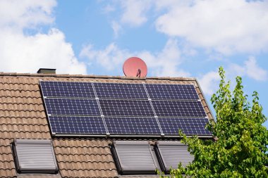 Photovoltaic system in full sunlight on a residential building roof. The dream of living in the countryside. A deciduous tree almost towers over the roof, but casts no shadow on the modules.