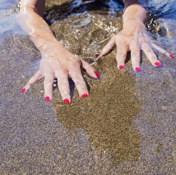 Mulher mãos na costa da água, areia preta — Fotografia de Stock