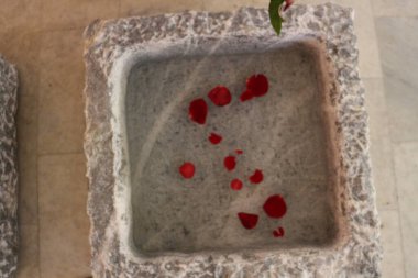 Gri taş havzada su içinde gül yaprakları