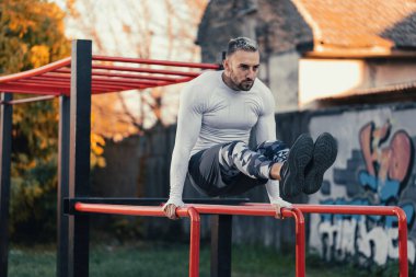 Yakışıklı adam mahalle spor salonundaki paralel barlarda kaslarını geliştiriyor. Açık hava konseptiyle çalışıyor.