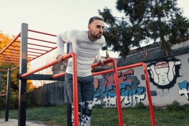 Paralel barlara dalan kaslı yakışıklı bir adam. Açık havada göğüs egzersizi.