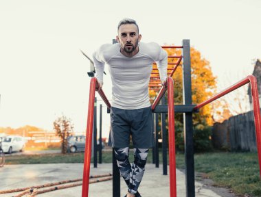 Paralel barlara dalan kaslı yakışıklı bir adam. Açık havada göğüs egzersizi.