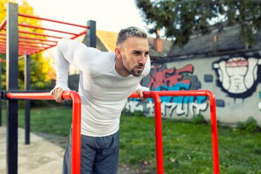 Paralel çubuklarda daldıran yakışıklı bir adam göğüs kaslarını spor konsepti dışında güçlendiriyor.