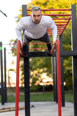 Paralel barlarda şınav çeken genç yakışıklı kaslı adam, egzersiz konsepti.