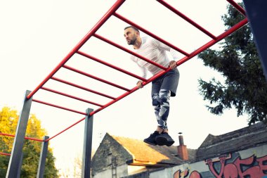 Yakışıklı kaslı genç adam gökyüzünün altındaki yatay merdivende çalışıyor. Açık hava sporu konsepti.
