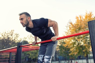 Yakışıklı bir adam, dışarıda spor yaparken vücudunu barın üzerine kaldırıyor. Sokak sporu ve sağlıklı yaşam tarzı konsepti. 