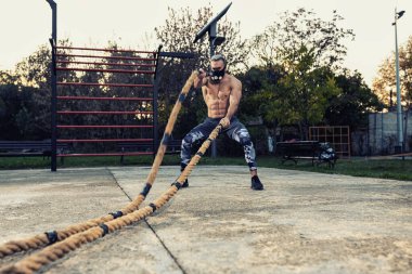 Savaş halatlarıyla antrenman yapan yakışıklı bir adam. Antrenman maskesi takıyor. Savaş halatları konsepti.