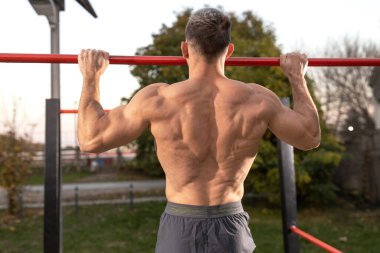 Yakışıklı adam barfiks çekiyor, arkadan görünüyor, spor salonunu kapatıyor.