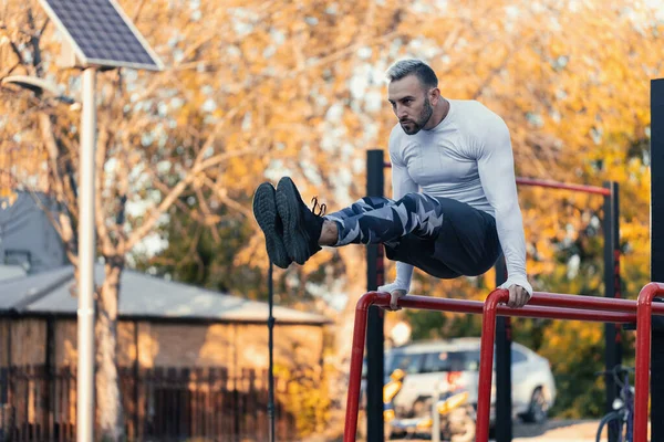 Kaslı bir adam paralel çubuklarda ön karın kaslarına vuruyor.