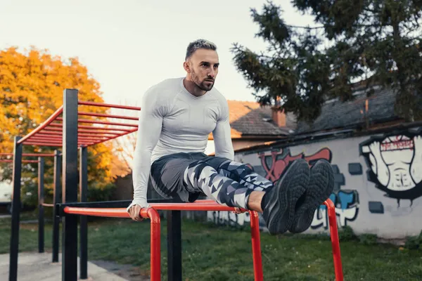 Genç kaslı yakışıklı adam kaslarıyla çalışıyor yatay merdiveni ve paralel bar istasyonunu kullanıyor.