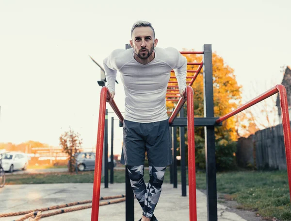 Paralel barlara dalan kaslı yakışıklı bir adam. Açık havada göğüs egzersizi.