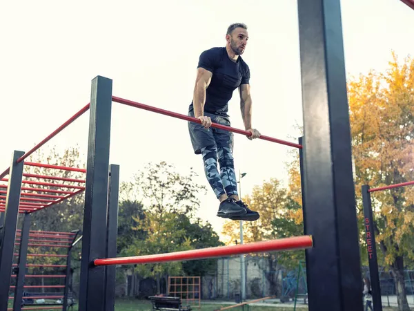 Genç kaslı adam dışarıda beden eğitimi yapıyor. Kendini barın üstüne kaldırıyor. Sokak jimnastiği konsepti.