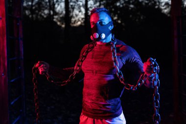 Güzel görünüşlü, güçlü, halter zincirleriyle parkta çalışan, yüksek irtifa simülasyon maskesi takan, dayanıklı ve dayanıklı bir adam.