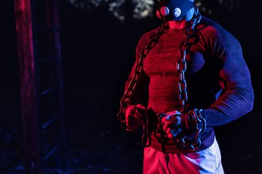 Antrenman maskeli yakışıklı kaslı bir adam. Geceleri parkta halter zinciri, gece konseptinde sokak sporu yapıyor. 
