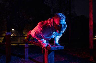 Solunum maskesi ve göğüs kasları egzersizi takan yakışıklı bir adam ahşap bankta şınav çekiyor.