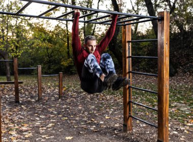 Yakışıklı kaslı adam elleriyle yatay bir rampaya tutunarak karın kaslarını çalıştırıyor, egzersiz yapıyor, karın kaslarını çalıştırıyor.
