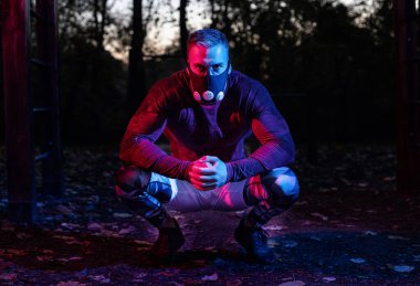 Spor maskesiyle yakışıklı genç bir adam parktaki konaklama pozisyonunda alacakaranlık seti gibi antrenmanlara ara veriyor, sıkı sokak antrenmanı konsepti. 