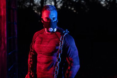 Antrenman maskeli yakışıklı kaslı bir adam. Geceleri parkta halter zinciri, gece konseptinde sokak sporu yapıyor. 