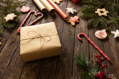 Noel hediyesi olarak, Noel süsü, şeker kamışı ve Noel kurabiyeleriyle birlikte ahşap bir masaya konan eko kâğıdı hediye. Mutlu Noeller konsepti.