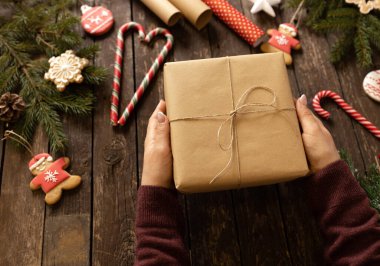 Noel hediyesini ahşap masanın üstünde, süslü kurabiyeler ve kozalaklı dallarla tutan kadın, bayram konsepti.