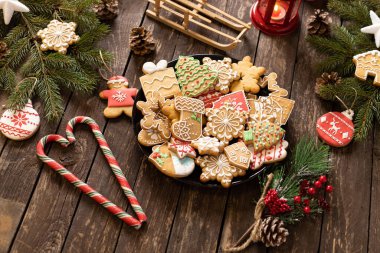 Tabak dolusu lezzetli ev yapımı kurabiyeler. Kış motifleri ve geleneksel Noel temaları ahşap bir kırsal masa arkasına yerleştirilmiş.