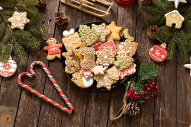 Kurabiyeler, şekerler ve bisküviler Noel süsü ve süslemeleri olan ahşap bir masaya yerleştirilmiş bir tabağa yerleştirilmiş şenlikli kış tatili şekilleri, kış tatili konsepti