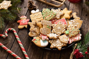 Geleneksel şekilli Noel kurabiyeleriyle dolu bir tabak şeker kaplı kış tatili temalarını Noel ve Yeni Yıl kavramları ile süslenmiş ahşap bir masaya koyun.  